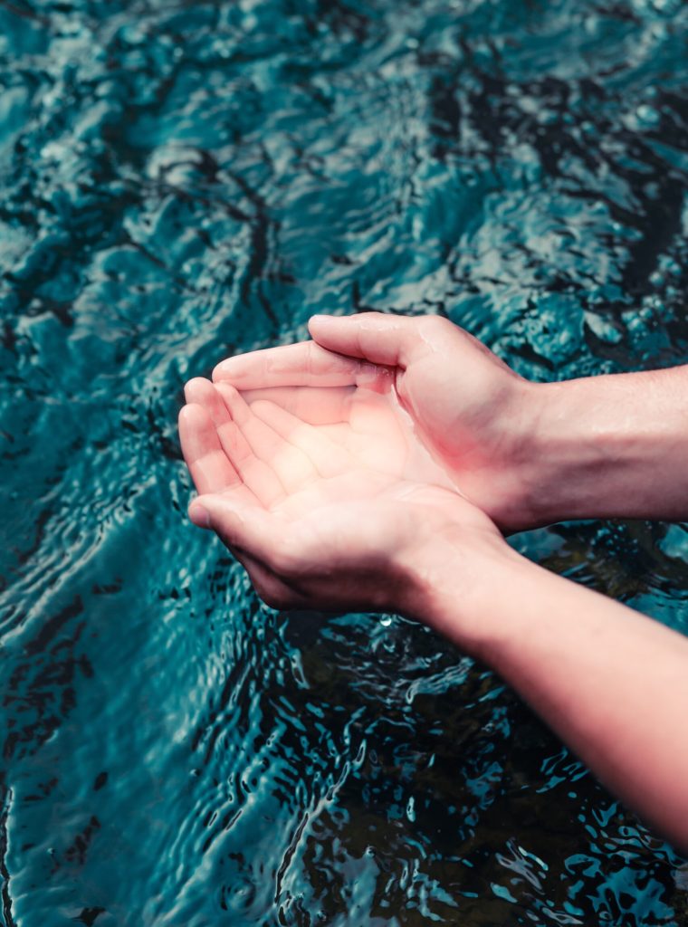 Young boy taking pure water from a river and holding it in the hands. Closeup of hands holding a clean water